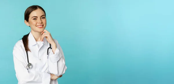 医务人员和医生的概念 年轻微笑的女医生 身穿白衣和听诊器的医护人员 看上去自信 等待病人 蓝色背景 — 图库照片