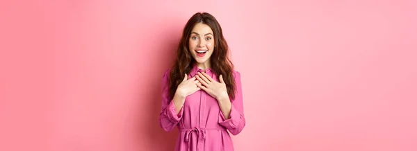 stock image Image of surprised and grateful young woman receive gift, holding hands on chest with flattered smile, saying thank you, being praised, standing over pink background.