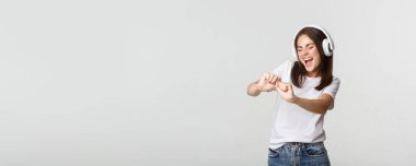 Neşeli genç bir kadın dans ediyor, kablosuz kulaklıkla müzik dinliyor..