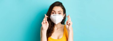 Sağlık, covid-19 ve tecrit konsepti. Solunum maskesi takan, dua eden, dua eden, dua eden, mavi arka planlı umut dolu genç bayanı kapatın..