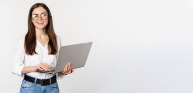 Portrait of young office woman, entrepreneur answer clients on laptop, working with computer with happy face, standing over white background.