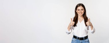 Happy smiling girl showing thumbs up, student with satisfied feedback, recommending smth, standing over white background.