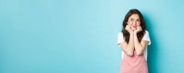 Tatlı, hayalperest kız bir şeyler hayal ediyor, elleri üzerine yaslanıyor ve sol üst köşeye bakıyor, hayal kuruyor, mavi arka planda duruyor..