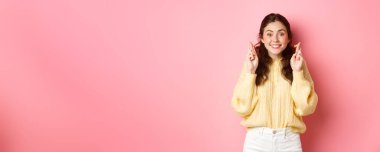 Güzel, neşeli bir kadının görüntüsü şans getirsin diye şans diliyor ve kameraya umutla bakıyor, dilek diliyor, pembe arka planda duruyor..