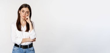 Unamused, bored brunette woman looking gloomy and sad, sighing, standing reluctant over white background.