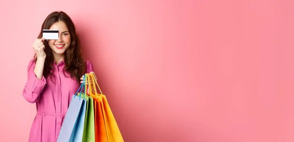 一个兴奋快乐的购物狂的画像 一个拿着购物袋 拿着塑料信用卡 面带微笑 站在粉色背景下的女人 — 图库照片