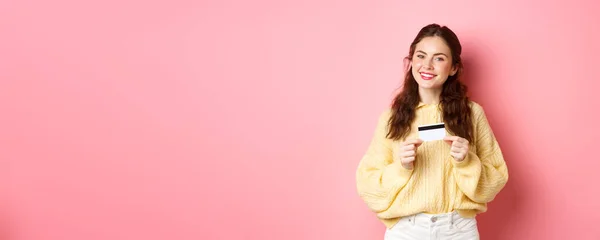 漂亮的女模特思维购物 手持塑料信用卡 面带微笑 站在粉色春光的背景下 复制空间 — 图库照片