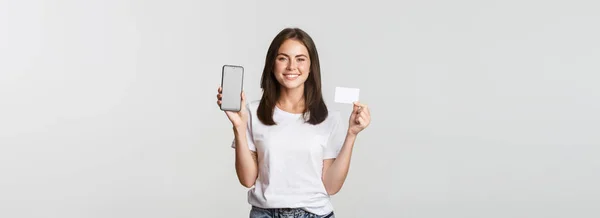 Приваблива Усміхнена Дівчина Виглядає Задоволеною Показує Кредитну Картку Екран Мобільного — стокове фото