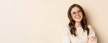 Close up portrait of young caucasian woman with dark hair, smiling white teeth, laughing, posing carefree against beige background.