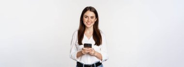 Young woman with smartphone, smiling and looking at camera, using mobile phone app, cellular technology and online shopping concept, white background.