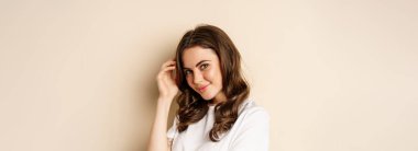 Close up portrait of coquettish beautiful girl gazing silly, gently smiling and giggling, posing flirty and cute against beige background. Women beauty and valentines concept.