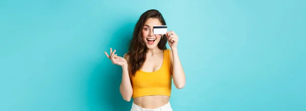 Stock image Excited beautiful woman in summer cropped top, look amazed at camera, shopping with credit card, standing over blue background.