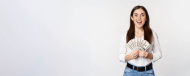 Portrait of beautiful woman holding money, cash, smiling pleased, standing over white background. Copy space