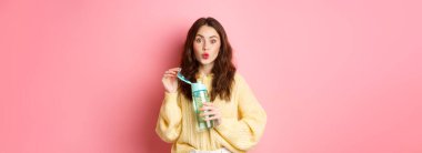 Heyecanlı esmer kadın portresi, kişisel spor şişesinden limon içen, ilgi çekici ve ilgili bakın kamera, pembe arka plan karşı duran.