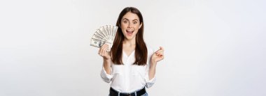 Enthusiastic woman showing money, cash and smiling, got loan, micro credit, standing delighted against white background.