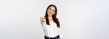 Confident young corporate woman pointing fingers at you camera, inviting, choosing, congratulating, standing over white background.