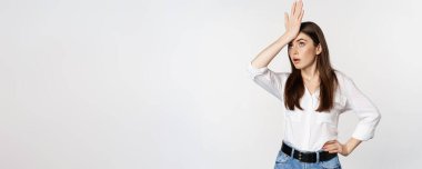 Annoyed young woman facepalm, slap forehead and roll eyes bothered, standing in white shirt and jeans over white background.