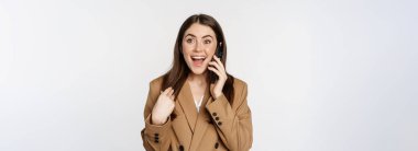 Enthusiastic businesswoman talking on mobile phone, reacting amazed and happy to call, recieve great news, standing over white background.