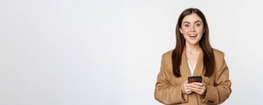 Smiling businesswoman using smartphone, app on mobile phone, standing over white background.