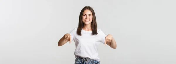 Spokojeně Usmívající Brunetka Dívka Ukazuje Prsty Dolů Doporučujeme Produkt — Stock fotografie