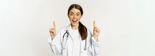 Entusiastiska Ung Kvinna Läkare Ler Pekar Finger Upp Bär Sjukhusuniform — Stockfoto