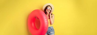 Stylish beach girl with swimming ring, laughing and smiling on summer vacation, sea trip, standing happy against yellow background.