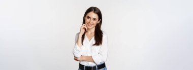 Smiling young businesswoman, female entrepreneur in white shirt, cross arms on chest like professional, standing over studio background.