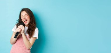 Mikrofon tutan, mikrofonda karaoke söyleyen, mavi arka planda duran güzel kız şarkıcı..