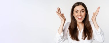 Enthusiastic young woman celebrating, smiling and raising hands up in rejoicing, winning and triumphing, standing over white background.