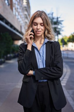 Kendine güvenen genç iş kadınının dikey görüntüsü. Telefon görüşmesi yapıyor, sokakta duruyor ve telefonla konuşuyor..