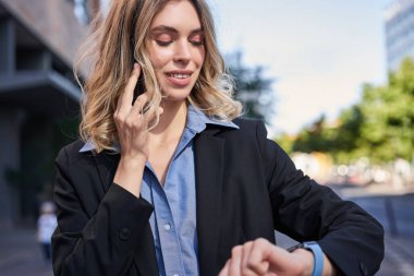 Kendine güvenen bir iş kadınının portresi toplantıya gidiyor, sokakta dikiliyor, cep telefonuyla konuşuyor ve dijital saati kontrol ediyor..