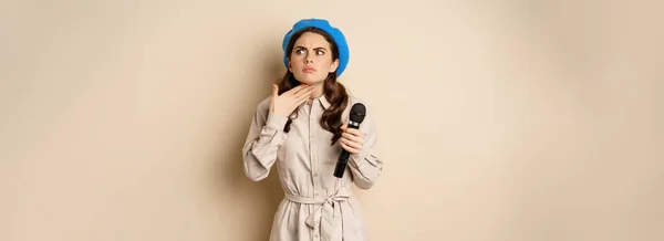 Stylish Singer Woman Microphone Touching Throat Feeling Ill Standing Beige — Stockfoto