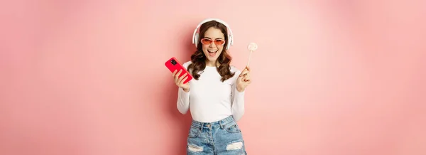 Mujer Bailando Gafas Sol Escuchando Música Auriculares Sosteniendo Piruleta Smartphone —  Fotos de Stock