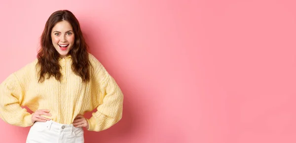 stock image Portrait of sassy and confident female model, holding hands on waist and smiling, saying yes with self-assured face, standing against pink background.