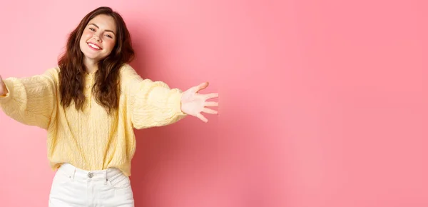 stock image Young beautiful woman reaching hands forward to hug you, smiling friendly, inviting for free cuddles, standing against pink background.