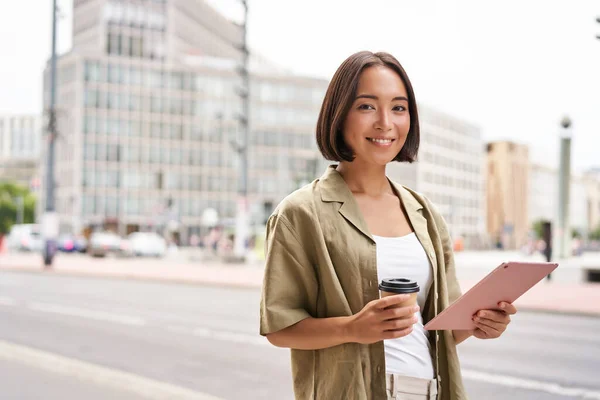 stock image Portrait of asian girl standing on street with tablet, drinking coffee.