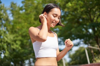 Sağlıklı olmak. Gülümseyen Asyalı fitness kızı, parkta koşan, gülümseyen ve koşan, sokaklarda koşu yapan.