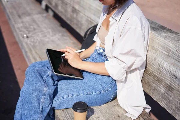 stock image Cropped shot of female hands holding pen, drawing on digital tablet, sitting on bench in park.