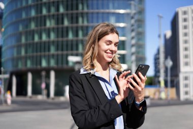 Şehir caddesinde cep telefonu kullanan kendine güvenen bir kadının portresi. İş kadını dışarıda dururken akıllı telefon uygulamasında mesajlaşıyor..