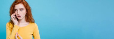 Yaşam tarzı kavramı - Kızıl kızıl saçlı kız arkadaşı ile cep telefonuyla konuşurken şok edici ve stresli ifade ile portresi. Pastel mavi arka plan üzerinde izole. Kopya alanı.