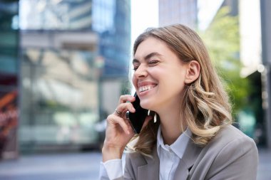 Cep telefonuyla konuşan, gülümseyen, sohbet sırasında gülen ve sokakta sohbet eden genç bir iş kadınının portresi..