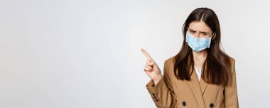 Coronavirus ve insanlar konsepti. Ofis kıyafetleri ve tıbbi yüz maskesi takmış üzgün, sol üst köşeyi gösteren, beyaz arka planı olan üzgün ve endişeli bir kadın..