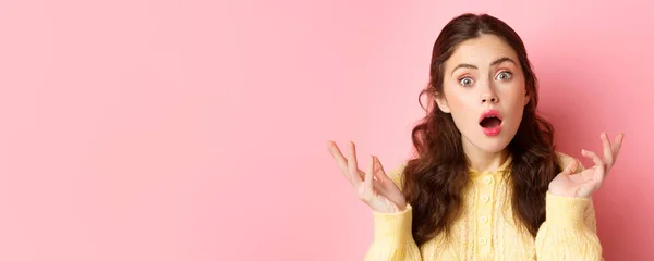 stock image Close up of surprised and confused young woman open mouth and raise hands, stare at camera puzzled, cant understand something, standing against pink background.