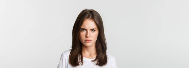 Close-up of pissed-off young girl frowning and looking angry at camera, white background.