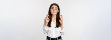Hopeful woman praying, cross fingers for good luck, begging, yearning smth, standing over white background. Copy space