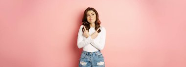 Complicated woman looking indecisive, stylish girl pointing fingers sideways and gazing thoughtful at upper left corner, making choice, deciding, pink background.