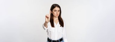Serious woman showing taboo, stop gesture, shaking finger in disapproval, disagree, forbidding something, standing over white background.