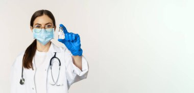 Genç kadın portresi, tıbbi maske ve üniformalı doktor, aşıyı gösteriyor, covid-19 aşı kampanyası, beyaz arka planda duruyor..