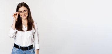 Portrait of female office worker, businesswoman looking at camera and smiling, standing over white background. Copy space