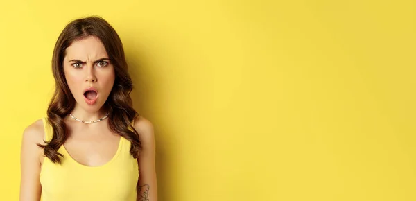 stock image Close up portrait of shocked young woman drop jaw, gasping and looking frustrated, standing against yellow background. Copy space